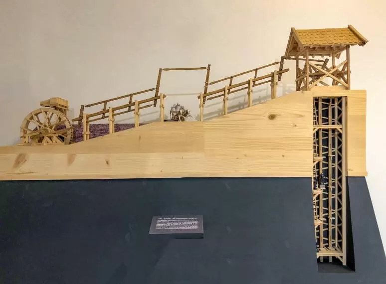 Modell einer historischen Bergbauanlage mit Förderband, Schaufelrad und Stollenstruktur, aus Holz gefertigt und in einem Ausstellungsraum präsentiert. 